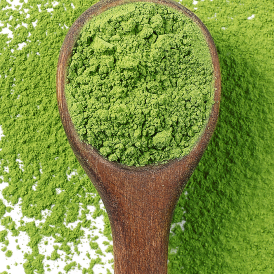 A wooden spoon of bright green KaLOHAS organic kale powder resting on fresh kale leaves
